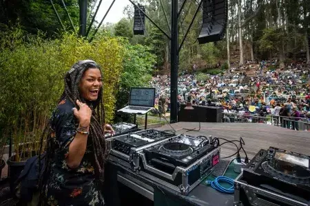 Una donna che fa il DJ allo Stern Grove Festival si guarda alle spalle e sorride alla telecamera.